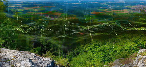 A landscape with trees, fields and cities can be seen with an overlay of a wave animation that is supposed to symbolize networking.