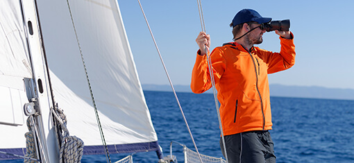 On a modern sailboat, a man with binoculars keeps a lookout.