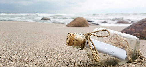 A message in a bottle lies in the sand on a deserted beach on a cold day under a slightly gray sky.
