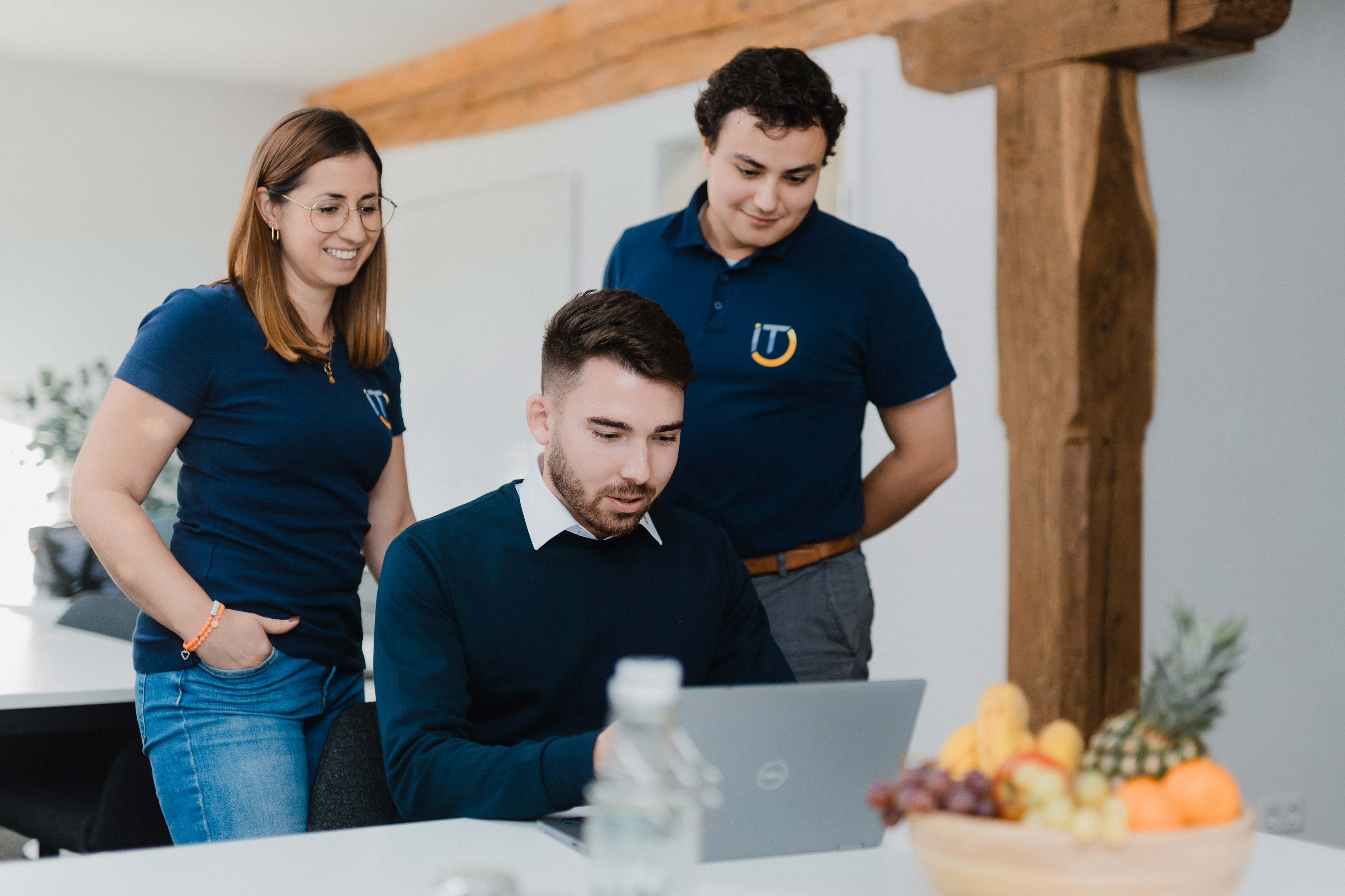 Slot A — Teamfoto aus dem Fotoshooting: drei IT-Kompass Mitarbeitende arbeiten gemeinsam und konzentriert an einem Laptop