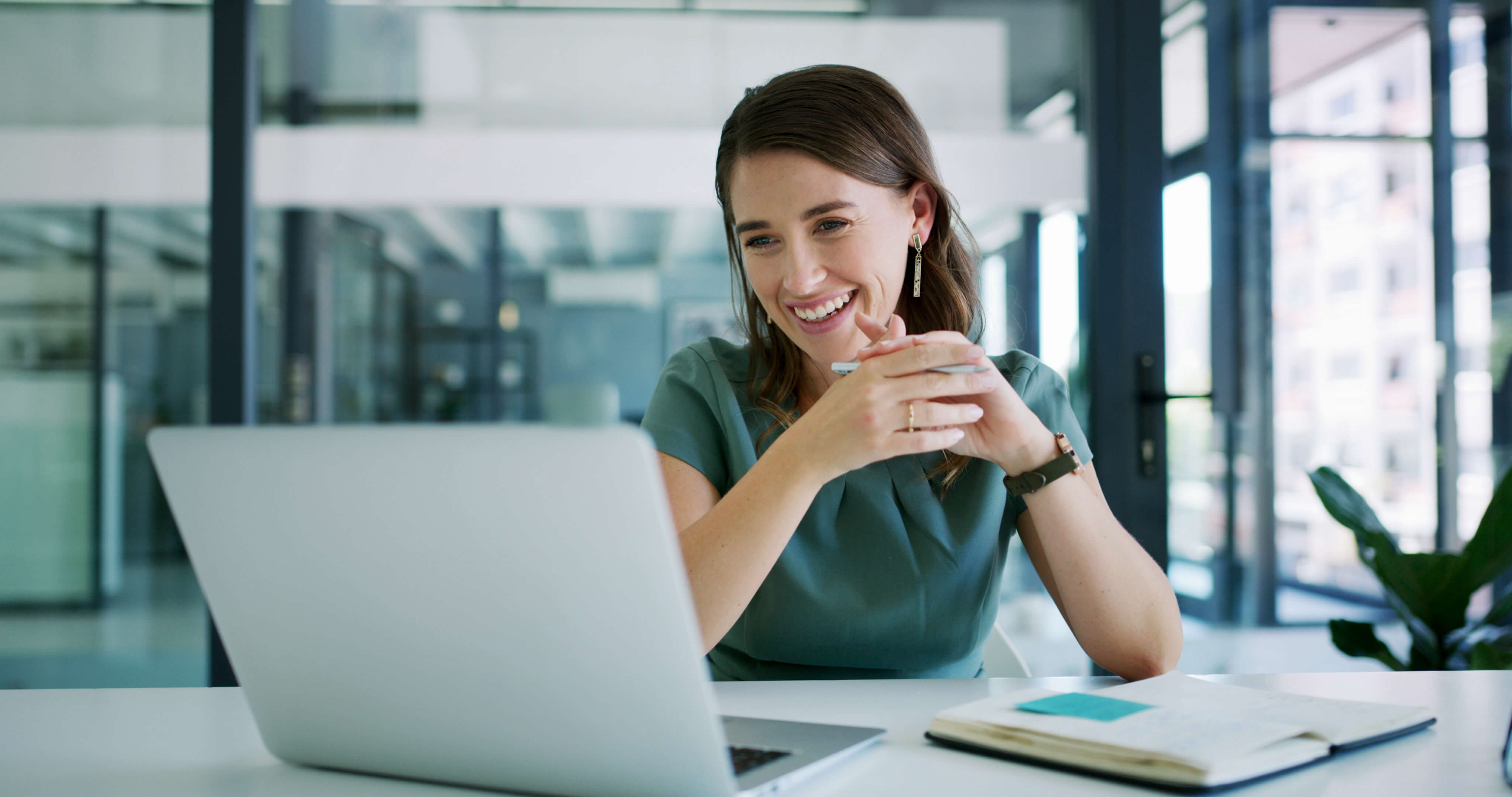 Lächelnde Frau liest am Laptop in einem hellen, modernen Büro