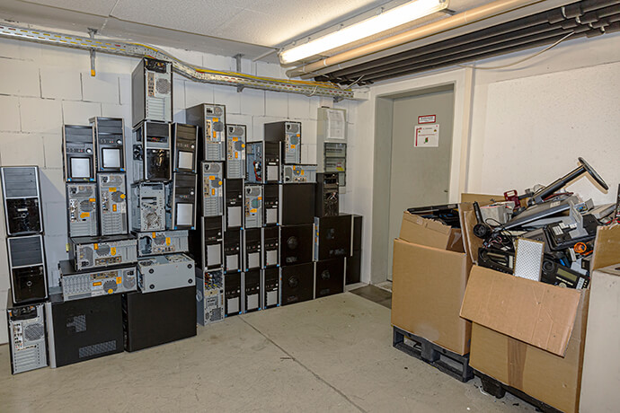 Computers and computer accessories are piled up in a basement storage room.